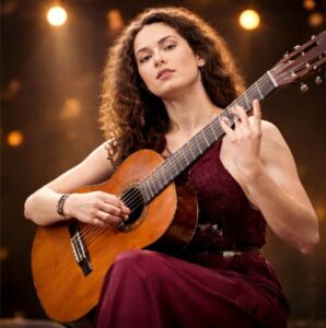 Sahne ışıkları önünde klasik gitar çalan kıvırcık saçlı bir kadın