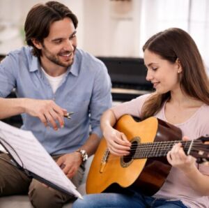 Bir erkek nota tutarken, gitar çalan genç bir kadına eşlik ediyor
