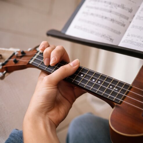 Nota standı önünde ukulele akoru basan bir elin yakın çekimi