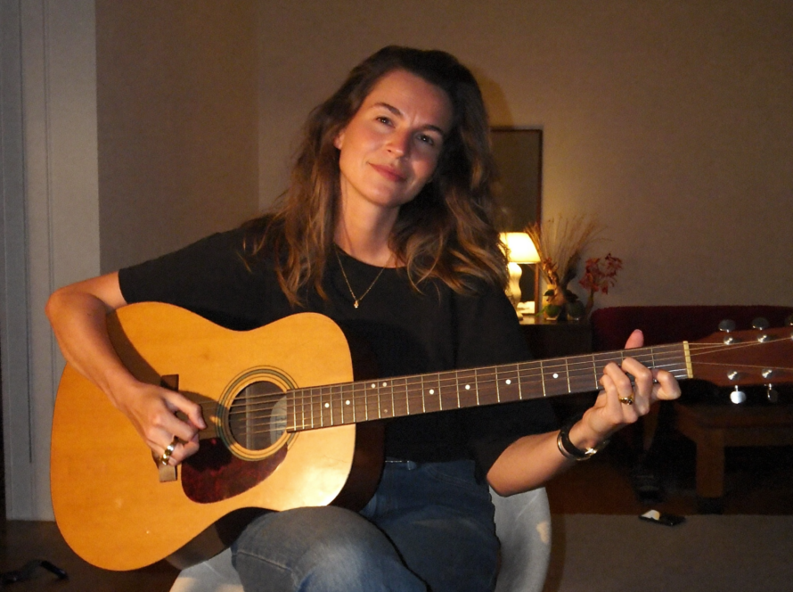 Evde akşam ışığında akustik gitar çalan yetişkin bir kadın